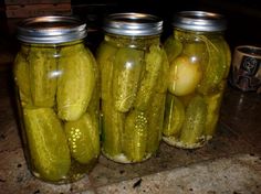 three jars filled with pickles sitting on top of a counter