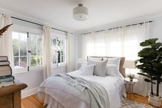 a bed with white sheets and pillows in a bedroom next to a window filled with books