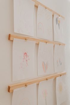 several children's drawings are hung on the wall with wooden pegs in front of them