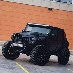 a black jeep is parked in front of a building with an orange wall behind it