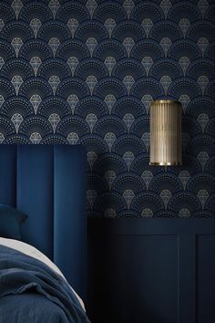 a bed with blue sheets and pillows in front of a wallpapered headboard