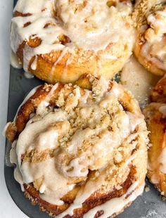 cinnamon rolls covered in icing on top of a baking sheet with crumbs