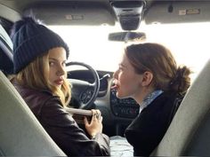 two women sitting in the back seat of a car, one talking to the other