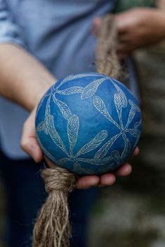 a person holding a blue ball with white designs on it's side and rope in their hands