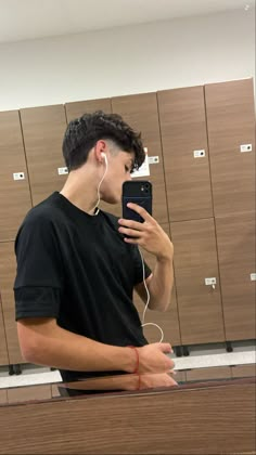 a young man is looking at his cell phone and listening to music while standing in front of lockers