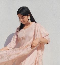 a woman in a pink dress is standing against a white wall and looking down at her hand