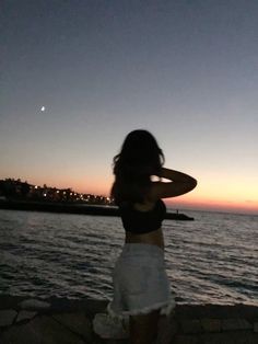 a woman standing next to the ocean at sunset