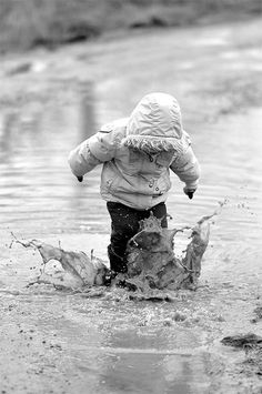 a young child playing in the water on a cold winter day, wearing a jacket and rain boots