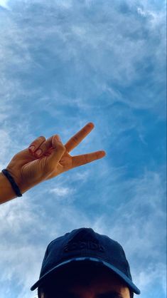 a man is making the peace sign with his hand while standing in front of a blue sky