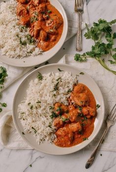 two plates filled with rice and meat next to silverware on a white tablecloth