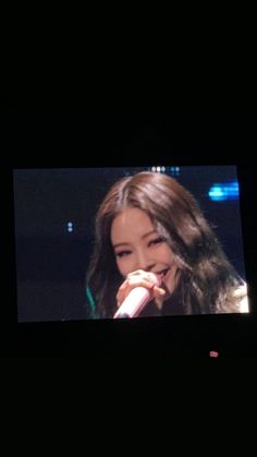 a woman with long dark hair is holding a microphone in front of her face while she sings