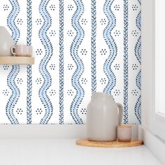 two vases on a shelf in front of a wallpapered background with wavy lines