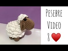 a crocheted sheep sitting on top of a table next to a red heart