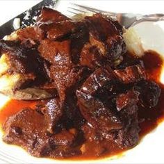 a white plate topped with meat and gravy next to a knife and fork