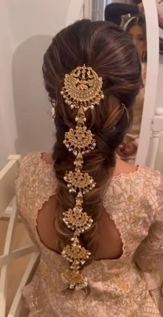 a woman with long hair wearing a gold headpiece in front of a mirror and looking at her reflection