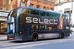 a black double decker bus driving down a street in front of tall buildings and shops