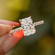 a close up of a person holding a ring with a princess cut diamond on it