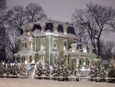 a large green house with snow on the ground and trees in front of it at night