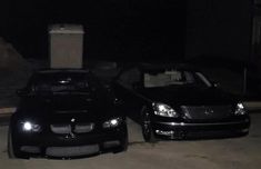 two black cars parked next to each other in the street at night with lights on