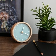 a clock sitting on top of a wooden table next to a potted plant and pen