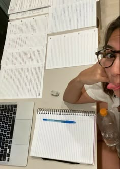 a woman sticking her tongue out while sitting at a desk with papers and laptop computer