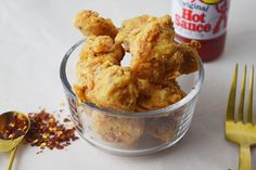 some fried food is in a small glass bowl next to a fork and mustard bottle