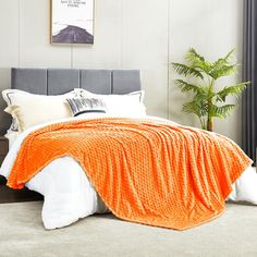 a bed with an orange blanket on top of it and a plant in the corner