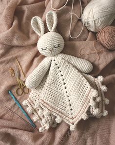 a crocheted bunny doll laying on top of a bed next to yarn and scissors