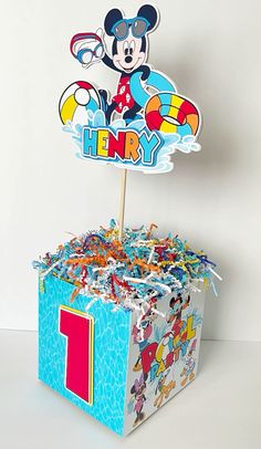 a mickey mouse cake topper sitting on top of a box filled with confetti