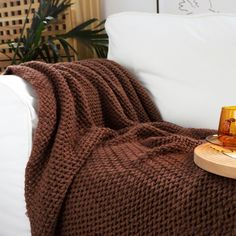 a brown blanket sitting on top of a white couch next to a wooden tray with an orange cup