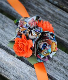 a bouquet made out of paper and orange ribbon on a wooden bench with an orange flower