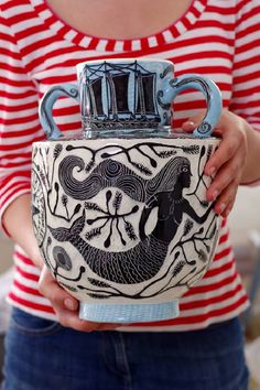 a woman is holding a vase with designs on it and her hands are in the air