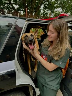 a woman in scrubs is petting a dog out the back of a car