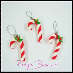 three red and white candy canes with green leaves hanging from silver chains on a white background