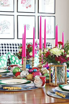 a dining room table set for christmas with pink candles and ornaments on the placemats