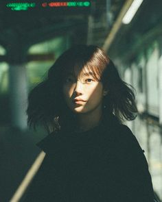 a woman standing in front of a train station with her hair blowing in the wind