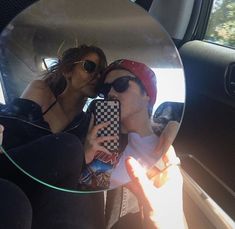 a man and woman taking a selfie in the back seat of a car with their cell phone