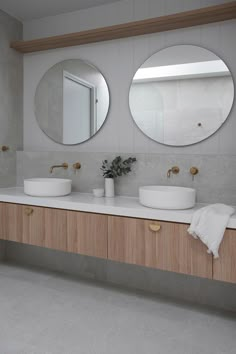 two round mirrors are above the sinks in this modern bathroom with wood cabinets and marble countertops