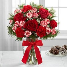 a vase filled with red and white flowers next to a pine cone on a table