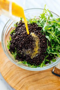 a glass bowl filled with black lentils and greens on top of a wooden cutting board