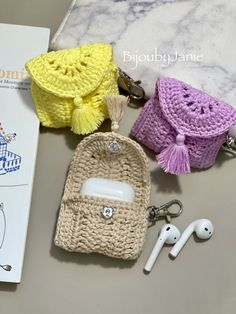 three crocheted purses and earbuds laying on a table next to a book