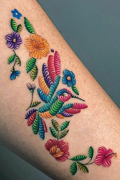 a woman's arm with colorful flowers and leaves painted on the back of it