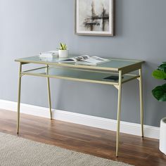 a desk with a glass top and metal legs in front of a gray wall next to a potted plant