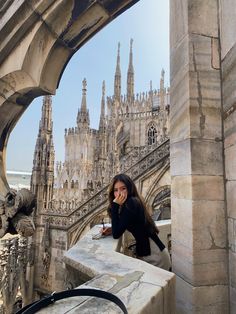 a woman standing on top of a stone building next to a tall tower with spires