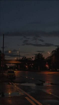 a city street at night with cars parked on the side of the road and traffic lights in the distance