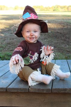 a baby wearing a witches hat sitting on a picnic table with her hands in the air