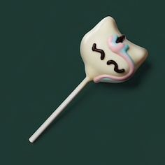 a white and pink lollipop with a face on it's side sitting on a green surface