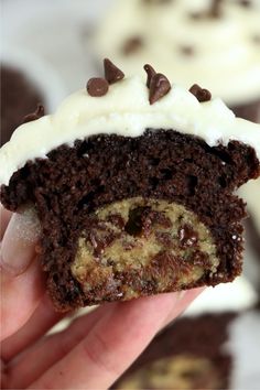 a hand holding a half eaten chocolate cupcake with white frosting and chocolate chips