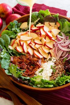 a salad with apples, onions, lettuce and cheese being poured into it