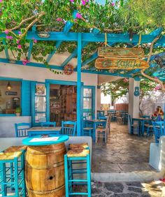 the outside of a restaurant with blue tables and chairs under a pergolated roof